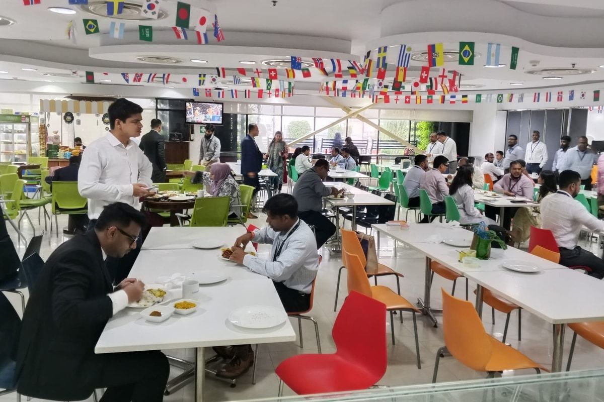 Office staff eating lunch at long tables in a corporate cafeteria run by Alpha Catering