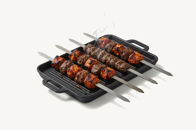 Skewers of beef and chicken tikka smoking on a black cast iron grill pan