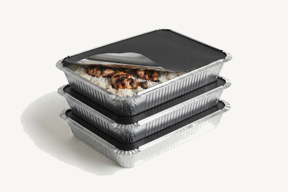 Three stacked foil trays with black lids, the top one peeled back to show grilled chicken skewers on rice