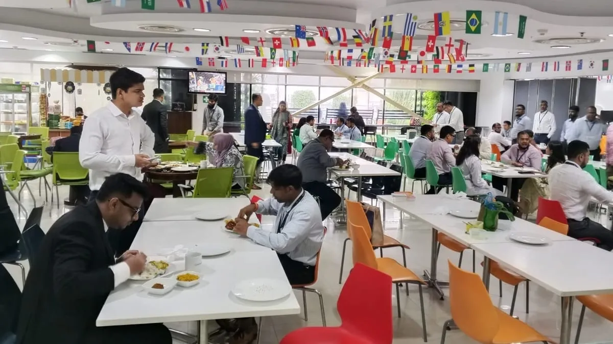 Staff serving lunch from a cafeteria counter with an item priced menu display at a corporate office in Dhaka