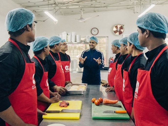 Cooks in hairnets and Alpha aprons at a steel prep table, with separate colour coded boards for raw meat and for vegetables